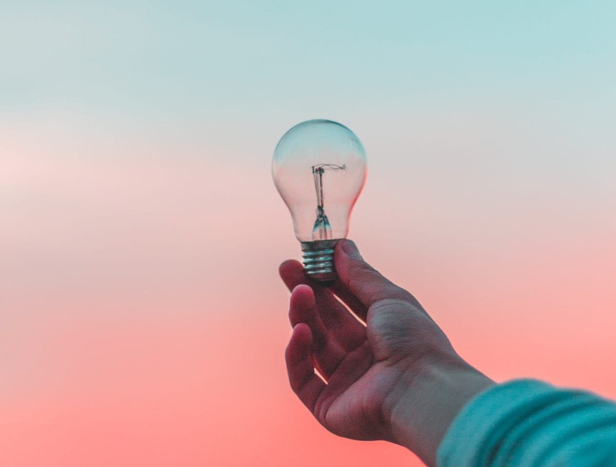 Someone holding up a Light bulb against blue fading into pink sky.