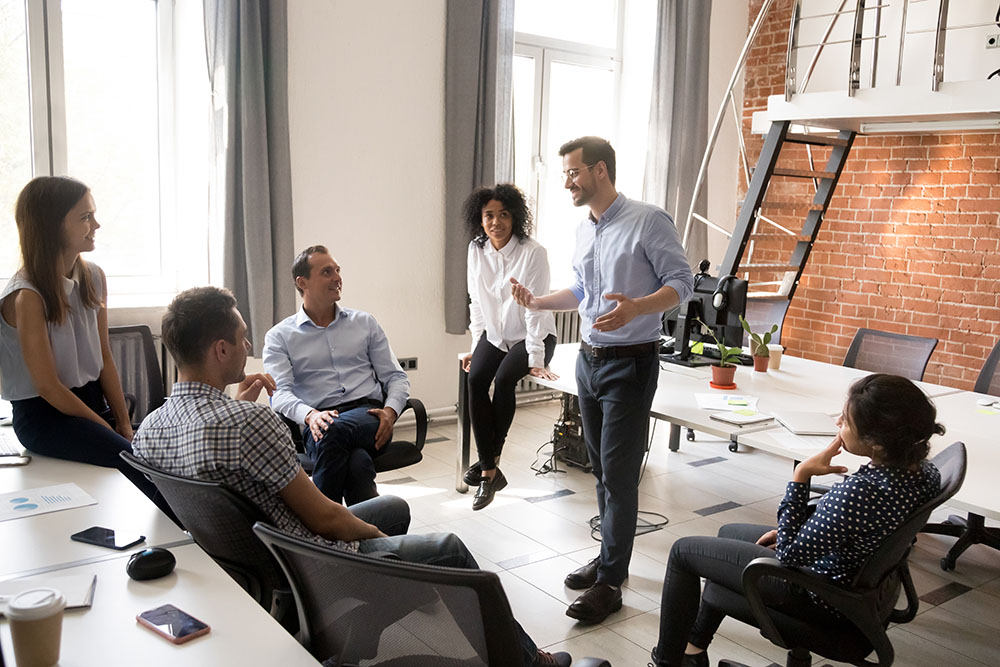 Confident leader, coach talking with multiracial group of office workers, having good conversation with subordinate, brainstorming, discussing business strategy, ideas, team building activity